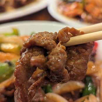 Beef dish with peppers and onions, held with chopsticks at Dragon Treasure